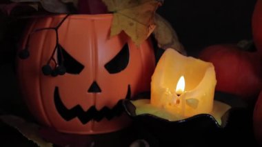 Mutlu Cadılar Bayramı. Bir mum Cadılar Bayramı için bir kompozisyon aydınlatır. Şeytani gülüşlü plastik bir balkabağı kovası, karanlıkta olgun balkabakları. Seçici odak