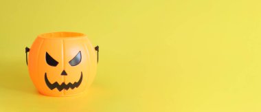 Mutlu Cadılar Bayramı. Sarı arka planda şeytani bir gülümsemesi olan plastik bir balkabağı kovası, mesaj için boş bir alan. Uzayı kopyala Cadılar Bayramı Afişi