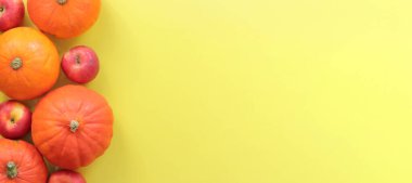 Sarı arka planda olgun balkabakları ve elmalar, üst manzara. Sonbahar hasat konsepti. Mevsimlik afişler için fotoğraflar. Ürünler masada. Boşluğu kopyala