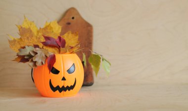 Mutlu Cadılar Bayramı. Şeytani bir gülümsemesi ve sonbahar yaprakları olan plastik balkabağı kovası, ahşap arka plan ve mutfak kesme tahtası. Cadılar Bayramı için kompozisyon