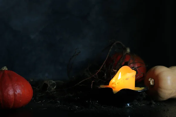 Happy Halloween. A burning candle, plant roots and pumpkins in the ground on a dark background. Gloomy Halloween composition for cards and banners