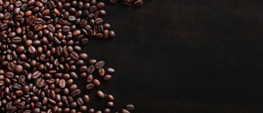 Ahşap, koyu bir masanın üstünde kavrulmuş kahve çekirdekleri. Yüzeye saçılmış kahverengi kahve çekirdeklerinin arka planı. kopyalama alanı. Metin için yer