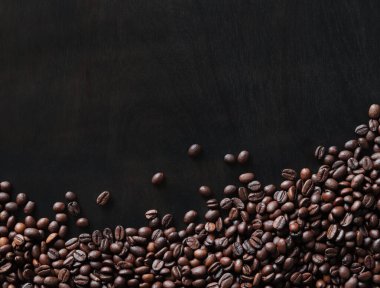 Ahşap, koyu bir masanın üstünde kavrulmuş kahve çekirdekleri. Yüzeye saçılmış kahverengi kahve çekirdeklerinin arka planı. kopyalama alanı. Metin için yer