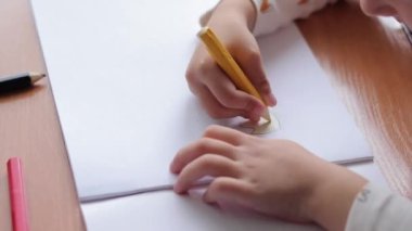 Bir albümde bir çocuk renkli kalemlerle resim çizer. Çocukların yaratıcılığı, anaokulunda, okulda ya da evde öğrenme. Kalemle yakın plan, seçici odaklı çocuk eli. Kız resim çiziyor.