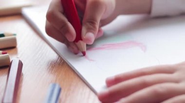 Bir anaokulu çocuğu bir albümde renkli kalemlerle resim çizer. Kalemle yakın plan, seçici odaklı çocuk eli. Kız renkli bir bulut çiziyor.