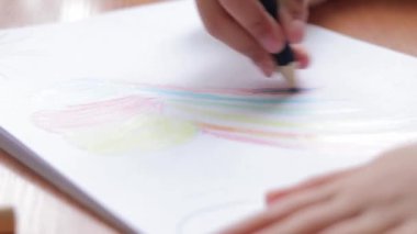 Bir anaokulu öğrencisi bir albümde renkli kalemlerle resim çizer. Kalemle yakın plan, seçici odaklı çocuk eli. Kız gökkuşağı çiziyor
