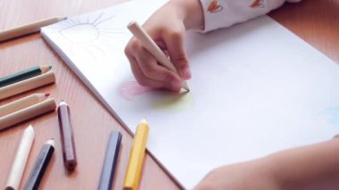 Bir anaokulu çocuğu bir albümde renkli kalemlerle resim çizer. Kalemle yakın plan, seçici odaklı çocuk eli. Kız renkli bir bulut çiziyor.