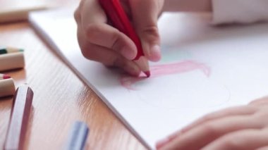 Bir anaokulu çocuğu bir albümde renkli kalemlerle resim çizer. Kalemle yakın plan, seçici odaklı çocuk eli. Kız renkli bir bulut çiziyor.