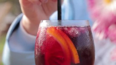 Sonbahar yağmurluklu bir kız bahçenin arka planına karşı sangria içer, açık hava kafesi. Cam kaplamalı kadın elleri var. Bir bardak sangria.