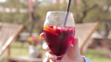 Sonbahar yağmurluklu bir kız bahçenin arka planına karşı sangria içer, açık hava kafesi. Cam kaplamalı kadın elleri var. Bir bardak sangria.