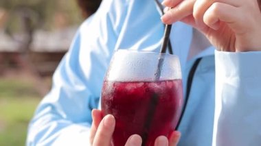 Sonbahar yağmurluklu bir kız bahçenin arka planına karşı sangria içer, açık hava kafesi. Cam kaplamalı kadın elleri var. Bir bardak sangria.