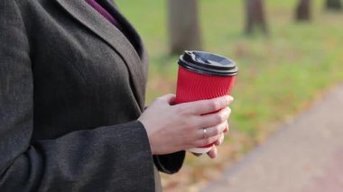 Sonbaharda bir kız parkta kahve ya da çay içer. Elleri kağıt bardakla yakın plan. Soğuk havada sıcak içecekler için. Bir fincan kahveli kadın elleri.
