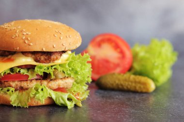 Gri arka planda duble çizburger ve sebze. Lezzetli hamburgerler yakın plan, yan manzara. Fast food