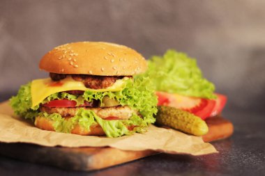 Gri arka planda duble çizburger ve sebze. Tahta kesme tahtasına yakın plan lezzetli bir hamburger. Fast food