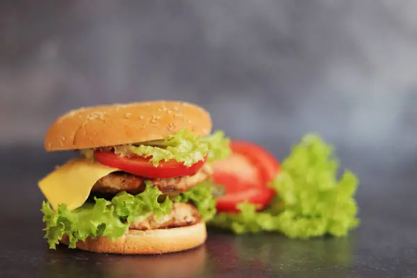Double cheeseburger and vegetables on a gray background. Juicy tasty burger close-up, side view. Fast food. Copy space