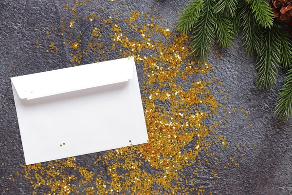 Open envelope on a gray textured background, gold sparkles, fir branch, top view, empty space. Copy space. Christmas branch and envelope for a letter or card