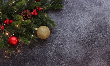 Yılbaşı topları ve gri arka planda parıldayan çelenklerle dolu bir dal, kopyalama alanı. Mesaj için yer. Yapay ladin dalı. Seçici odaklanma. Yeni Yıl Kompozisyonu
