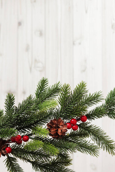 Christmas fir branch with decor and pine cone on a light wooden background, copy space. Place for text. Artificial spruce branch. Selective focus