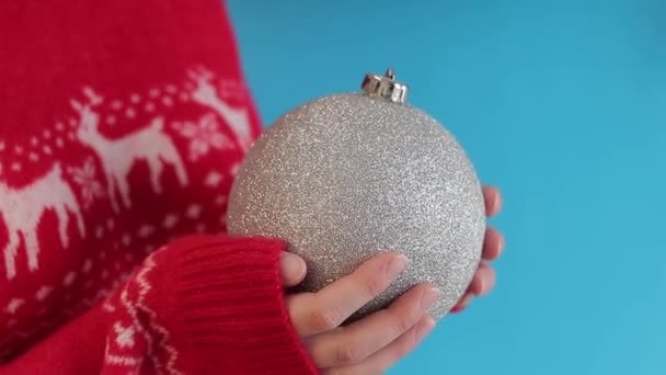 女性の手 クリスマスの装飾 赤い編まれたセーターの大きい銀のクリスマス ボール クリスマスの装飾 クリスマスツリーのおもちゃのクローズアップ 休日のための準備 — ストック動画