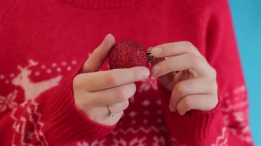 Kadınların elinde kırmızı, parlak bir Noel balosu, Noel süsü, yeni yıl. Noel dekoru, Noel ağacı oyuncağı yakın plan. Tatile hazırlanıyorum. Geyikli, kırmızı yılbaşı kazaklı bir kız.