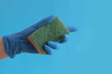 Elde sünger, odada ıslak temizlik, parlak mavi arka plan. Tabakların çeşitli yerlerini temizlemek için süngerli eldiven giymiş bir kadın eli. Temizlik. Bulaşıkları yıka. Ev hanımı.