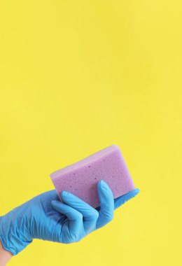 Sünger yakın plan. Bulaşık yıkamak için sünger ya da ıslak temizleme için sarı arka plan kullanan mavi lateks eldivenli bir kadın eli. Temizlik servisi