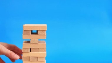 Bir kadın mavi parlak arka planda Jenga oynuyor. Aile tatili, tatiller, eğlence. Bir kadının eli, tahta oyuncak kulesinden bir blok ötede. Oyun