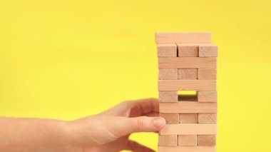 Sarı arka planda Jenga oynayan bir kadın. Aile tatili, tatiller, eğlence. Bir kadının eli, tahta oyuncak kulesinden bir blok ötede. Bir oyun