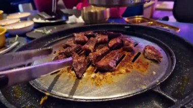 Kore restoranında biftek pişirmek, eti pişirmek için teslim etmek, yakın plan. Kore barbeküsü. Kore restoranındaki demir ızgara tavasında et kızartıyoruz. Kömürde pişirmek. Kızarmış et.