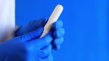 Bir kadının elindeki mukavva aplikatörde tampon, mavi arka plan. Mavi lateks eldivenli bir elin tamponu olur. Kadınsı kişisel hijyen ürünleri. Jinekolog.
