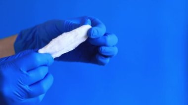 Mavi arka planda tamponu olan bir kadın eli. Mavi lateks eldivenli bir elin tamponu olur. Kadınsı kişisel hijyen ürünleri. Jinekolog.