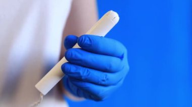 Bir kadının elindeki mukavva aplikatörde tampon, mavi arka plan. Mavi lateks eldivenli bir elin tamponu olur. Kadınsı kişisel hijyen ürünleri. Jinekolog.