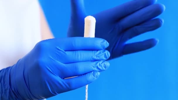 青い背景にタンポンのクローズアップを施した女性手 青いラテックスの医療用グローブの手がタンポンを保持しています 女性の衛生製品 ガインコロジスト — ストック動画