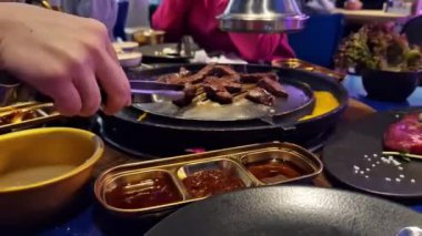 Kore restoranında sığır eti pişiriyorum, yakın plan. Kore barbeküsü. Kore restoranındaki demir ızgara tavasında et kızartıyoruz. Kömürde pişirmek. Kızarmış et.