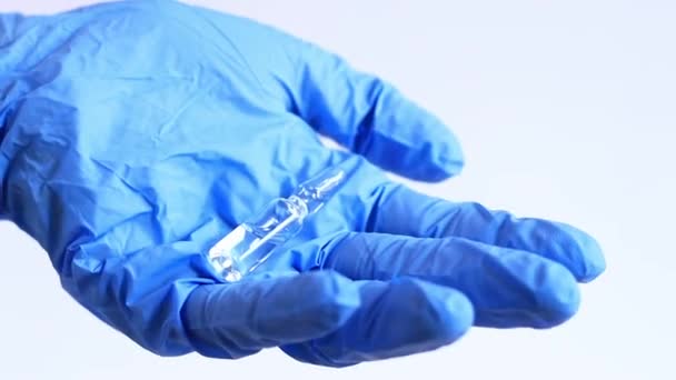 青い医療用グローブの女性の手は 薬でガラスアンプルを保持しています 軽い背景に抗生物質またはワクチンが付いているガラス アンプル 医者や看護師が手元に薬を持っている — ストック動画