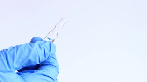 青いメディカルグローブの女性の手は ガラスアンプルを保持しています 軽い背景に抗生物質またはワクチンが付いているガラス アンプル 医者や看護師が手元に薬を持っている — ストック動画