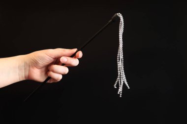 Elinde koyu arkaplanda metal toplar olan dekoratif bir kırbaç var. Bir kadının elinde seks aksesuarı. Seks oyuncakları, seks dükkanı konsepti