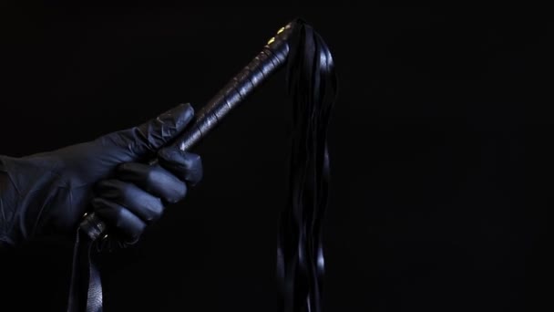 一只戴着黑色乳胶手套的手拿着鞭子在深色背景下抽 用皮革鞭子抽打孤立在黑色上 性玩具的亲密 性奴役 — 图库视频影像