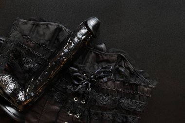 Sex toy, top view. Huge black dildo on a women's sexy corset, black background. Items for sexual games. Black sex toy, artificial phallus on a dark background. Flat layout