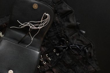 Siyah debriyaj çantası, dekoratif kamçılı, korse üzerinde metal toplar, koyu arka plan, üst manzara. Seks oyunları için seksi kırbaç kıyafeti. Cinsel uyarılma için eşyalar