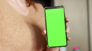 Bir kadının eli yeşil ekranlı bir telefonu tutuyor. Chroma anahtarı, akıllı telefon teknolojisi, bir kadının elindeki cep telefonu bir apartmanın arka planında. Cep telefonu tutan bir kadının yakın çekimi.