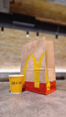 Kyiv, Ukrayna - 28 Şubat 2024: Üzerinde McDonalds 'ın fast food restoranı logosu ve masada bir fincan kahve olan bir kese kağıdı. McDonald 's için paket poşeti ve paket yiyecek.