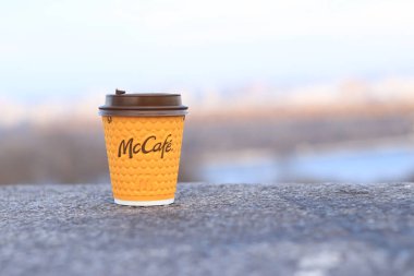 Kyiv, Ukrayna - 28 Şubat 2024: McCafe içecekleri için kağıt bardak. Fast food restoranından bir şeyler içmek. Bulanık bir şehrin arka planında McDonalds 'dan gelen kahveli tek kullanımlık sarı bir kupa.