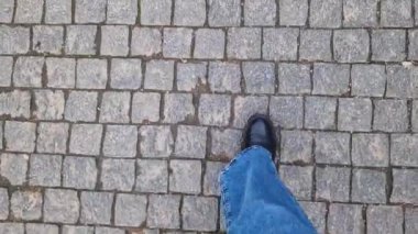 Kadın ayakları kaldırım taşı patikasında yürüyor, birinci şahıs görüşü. Sokakta yürürken insan ayağına yakın çekim. Baharda ya da sonbaharda güneşli bir günde yürüyüş. Tarihi taş kaldırım taşı sokağının en üst manzarası