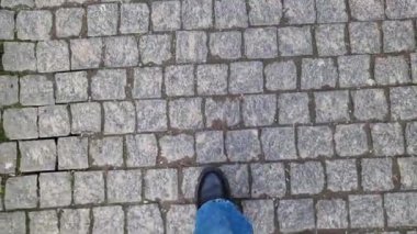 Kadın ayakları kaldırım taşı patikasında yürüyor, birinci şahıs görüşü. Sokakta yürürken insan ayağına yakın çekim. Baharda ya da sonbaharda güneşli bir günde yürüyüş. Tarihi taş kaldırım taşı sokağının en üst manzarası