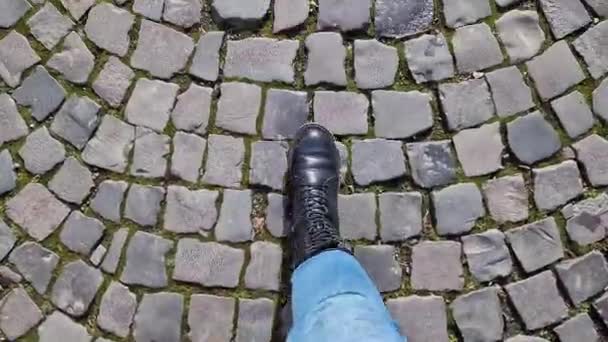 青いジーンズの女性の足は 石畳の道を歩いています ファーストパーソンビュー 通りを歩いている人間の足の閉鎖 歴史ある石造りの石造りの石造りのストリートのトップビュー — ストック動画