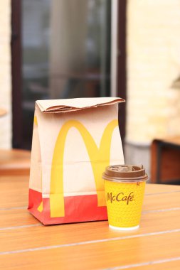 Kyiv, Ukrayna - 19 Mart 2024: Üzerinde McDonalds 'ın fast food restoranı logosu ve sokaktaki masada bir fincan kahve olan bir kağıt torba. Bulanık arka planda paket yemek torbası. Latte