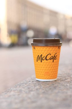 Kyiv, Ukrayna - 19 Mart 2024: Caddelerde McDonald 's fast food restoran logosu olan kağıt latte bardağı. Arka planda bulanık bir kahve. Tek kullanımlık sarı karton bardakta Latte. Kahve içmeye.