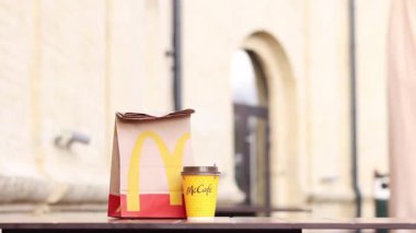 Kyiv, Ukrayna - 19 Mart 2024: Üzerinde McDonalds 'ın fast food restoranı logosu ve sokaktaki masada bir fincan kahve olan bir kağıt torba. Bulanık arka planda paket yemek torbası. Latte