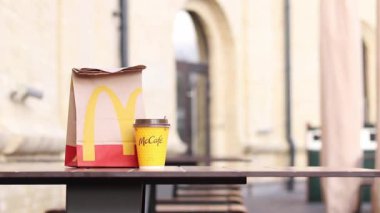 Kyiv, Ukrayna - 19 Mart 2024: Üzerinde McDonalds 'ın fast food restoranı logosu ve sokaktaki masada bir fincan kahve olan bir kağıt torba. Bulanık arka planda paket yemek torbası. Latte